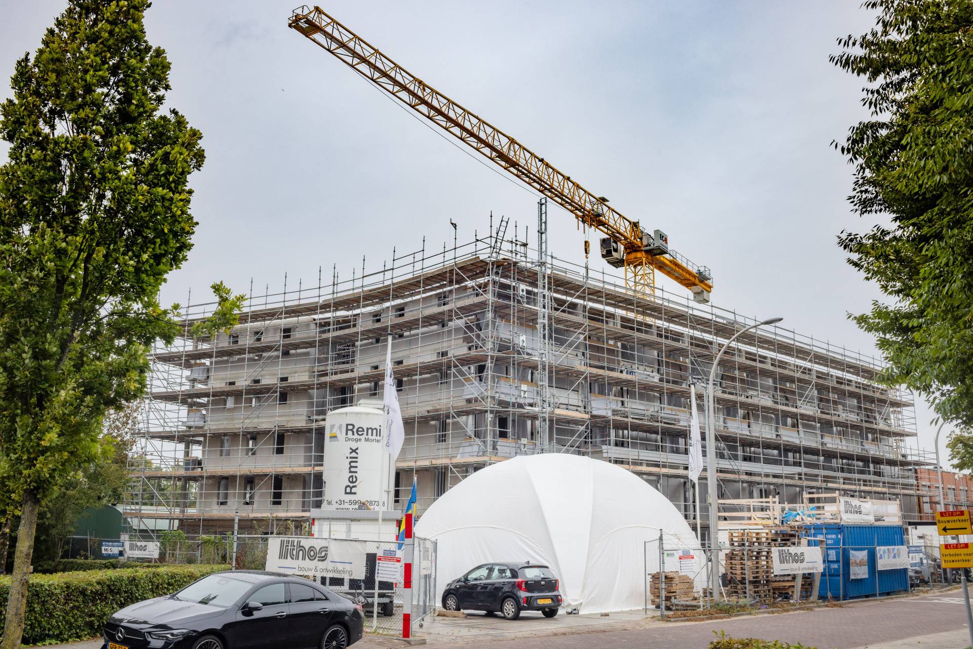 Nieuwbouwplaats met hijskraan en steigers.